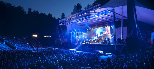 Blue lit open air stage with large audience