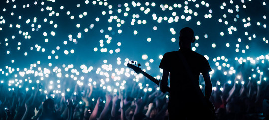 Bass guitarist plays to the crowd of big stadium with flashing lights